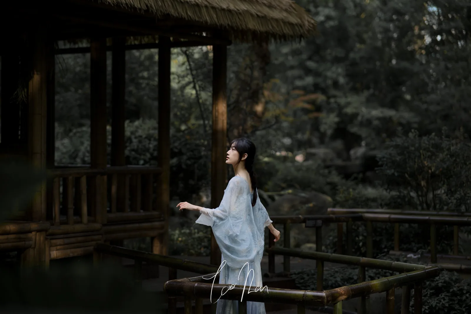 A person in pale clothing standing among a wooden pavilion and trees