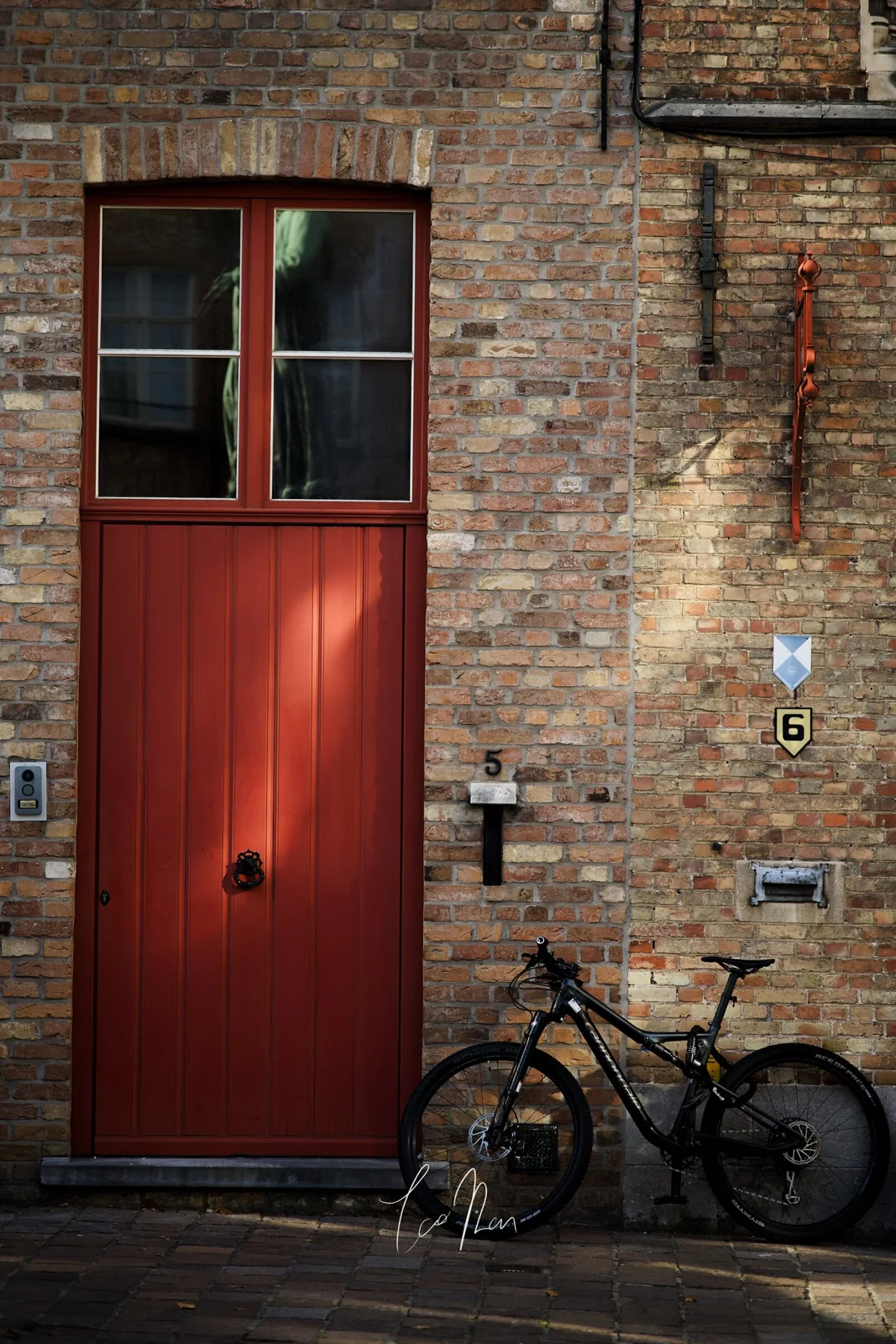A red door and bicycle against a brick wall